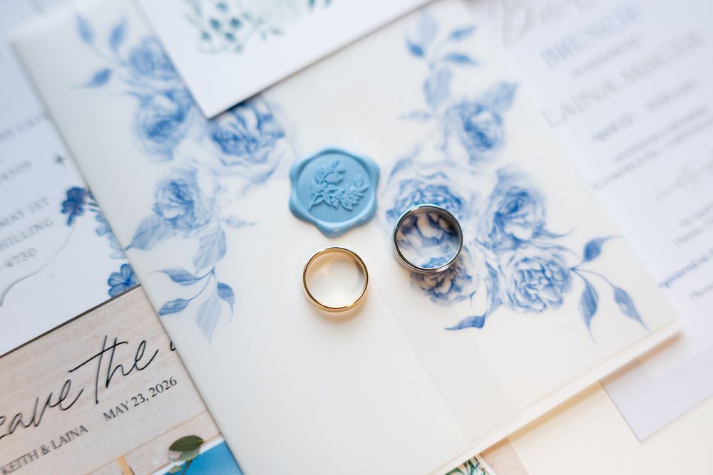 Wedding rings and blue floral stationery suite with wax seal displayed on elegant invitation set.