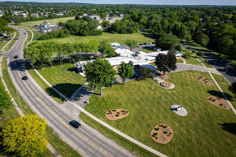 Aerial view of a green park with circular garden beds beside a road, surrounded by trees senior living facility, drone photography