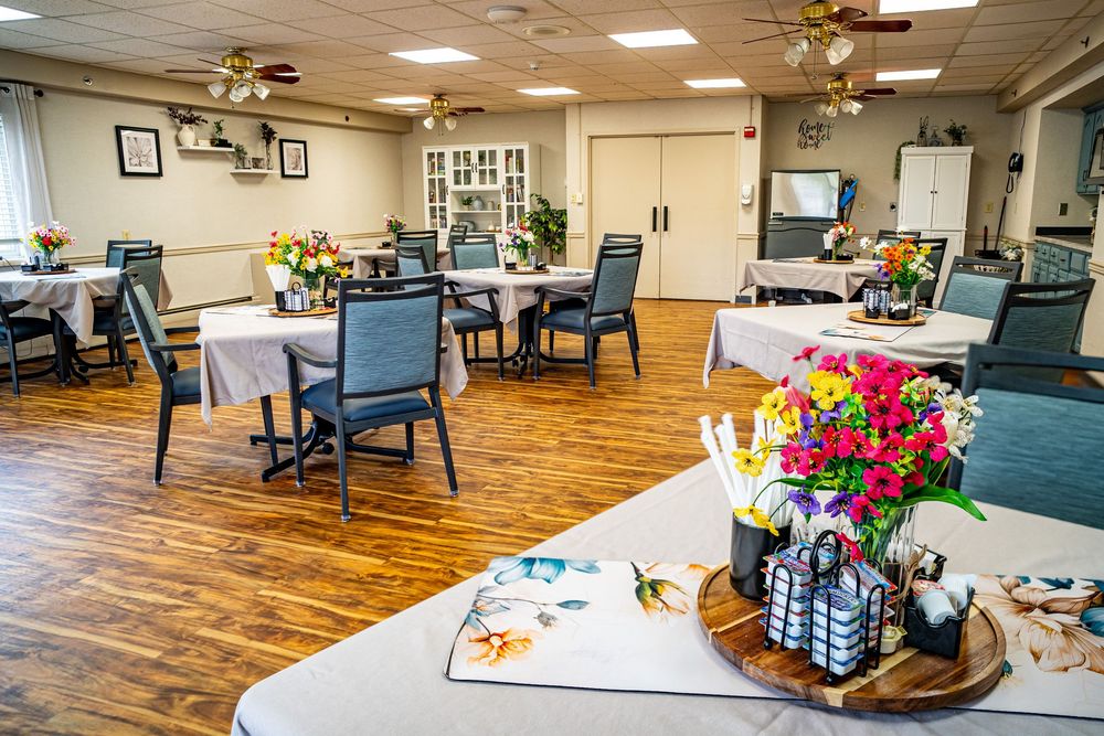 Bright dining room with white tablecloths, colorful floral centerpieces, and hardwood floors in a senior living facility. branding photo