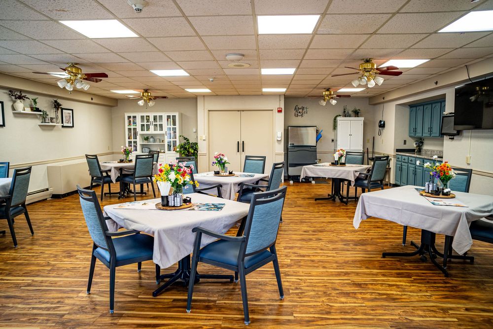 Bright dining room with round tables, blue chairs, hardwood floors, ceiling fans, and floral centerpieces. interior real estate photography