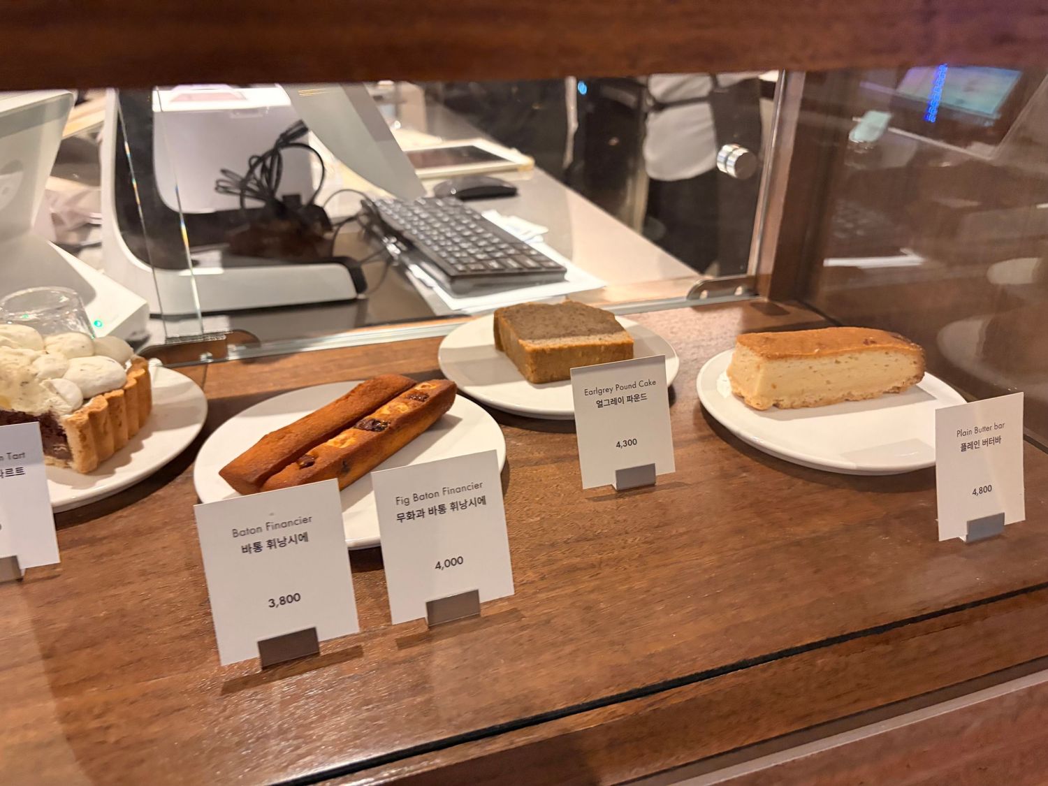 Bakery display case showcasing assorted pastries and breads on white plates with price tags in an Asian café.