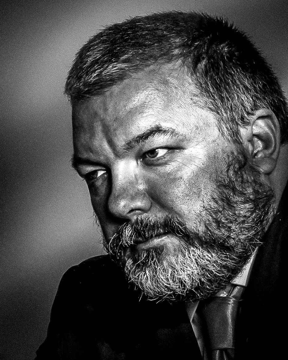 Black and white portrait of a bearded middle-aged man with a serious expression, dramatic lighting.