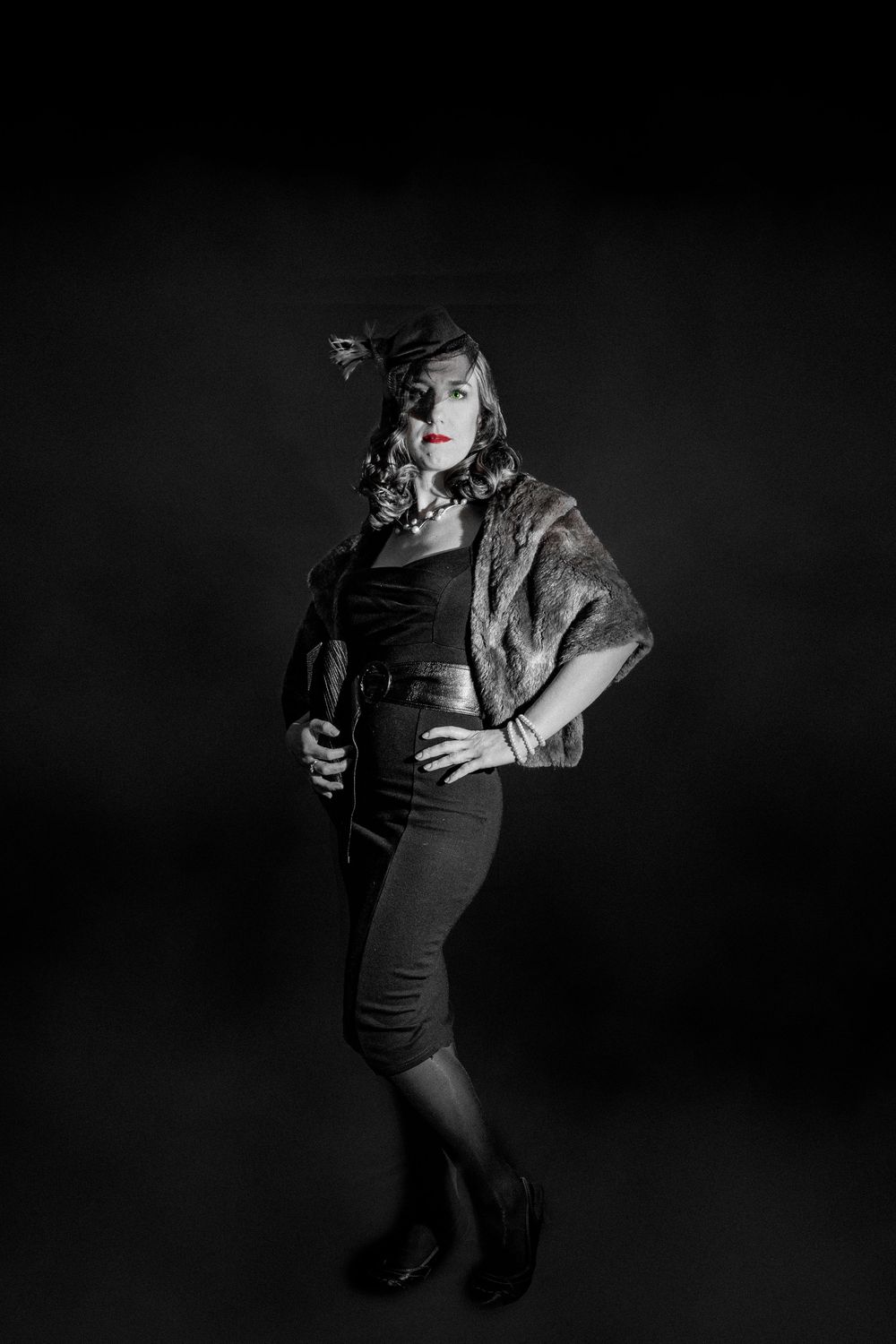 Black and white vintage portrait of a woman in fur stole and fascinator hat with red lips, studio photography.