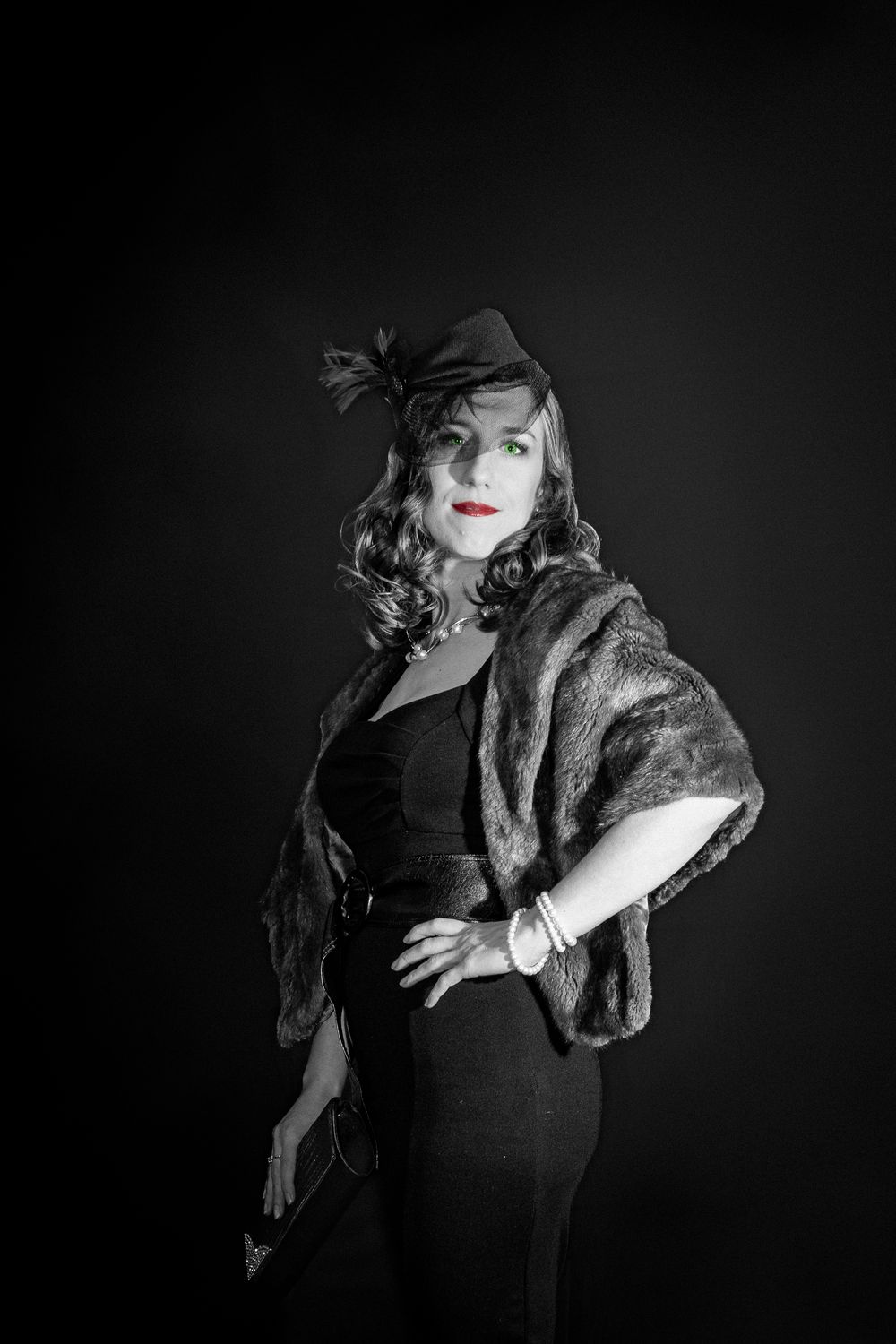 Black and white portrait of an elegant woman in vintage attire, fur stole, and feathered hat against dark background.