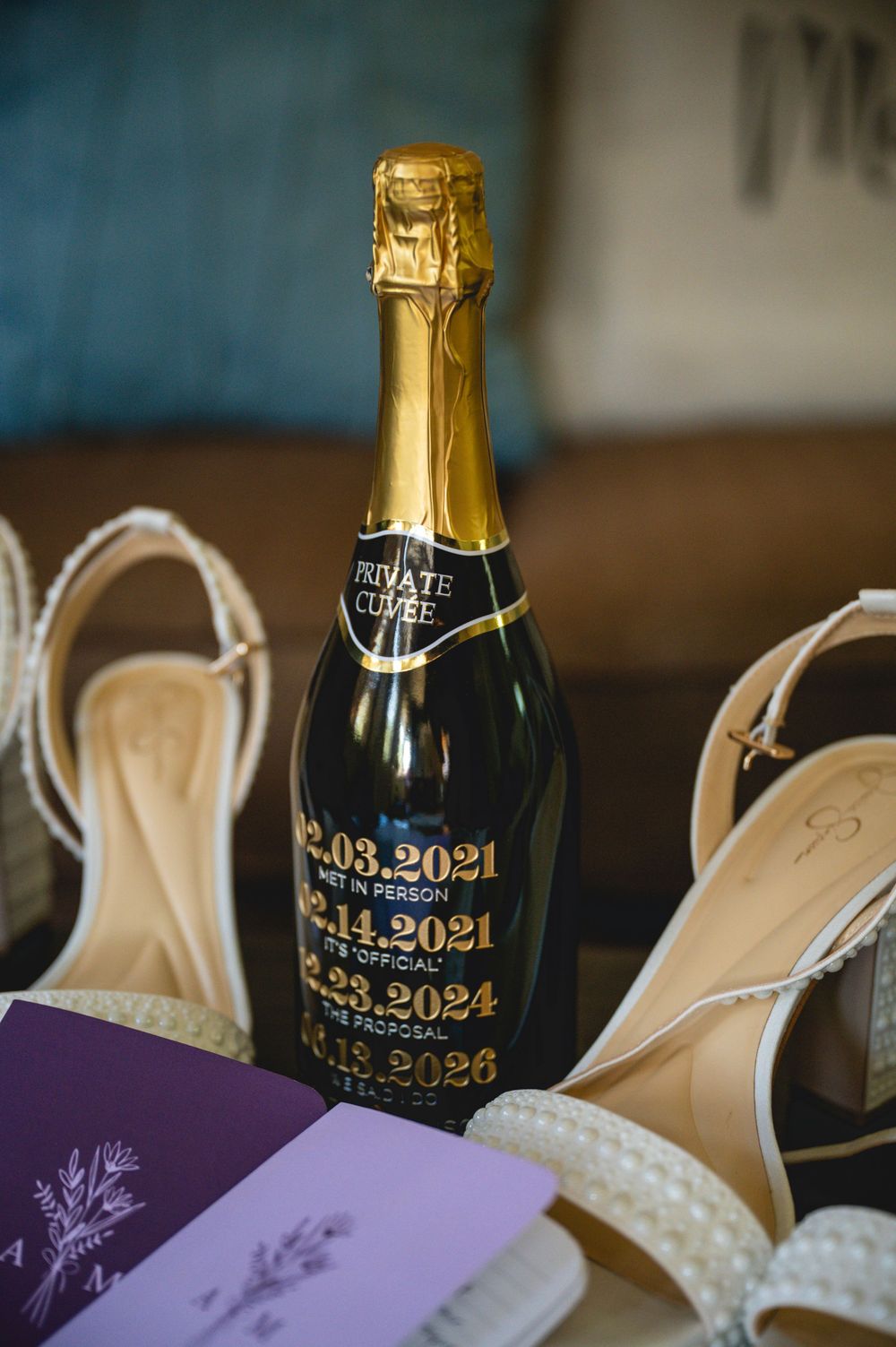 Custom engraved champagne bottle with wedding dates displayed alongside pearl heels and lavender stationery.