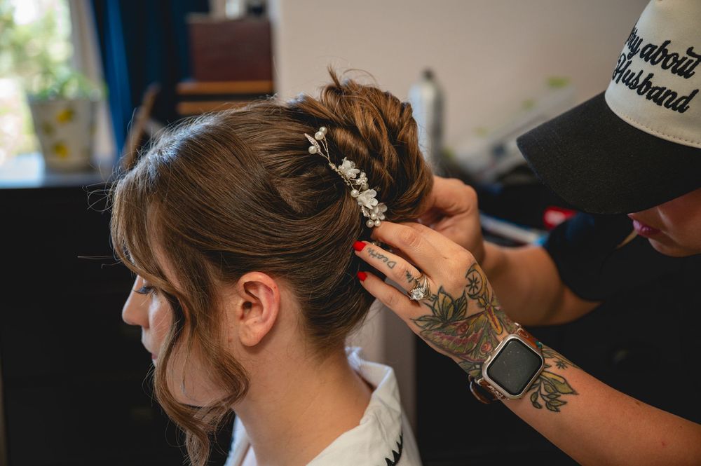Tattooed hairstylist adding floral hair accessories to a brunette updo bridal hairstyle.