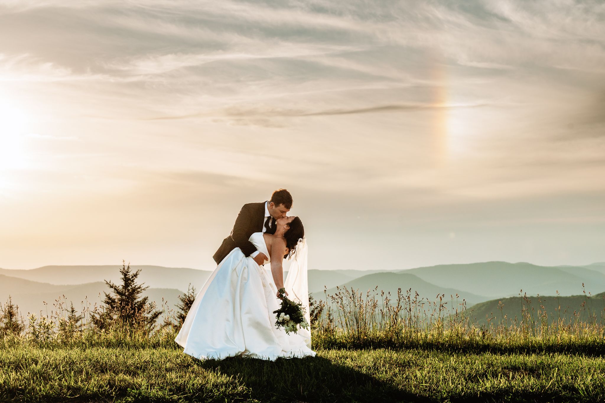 Bride + groom share a dip kiss at sunset under a rainbow on Snowshoe Mountain in West Virginia