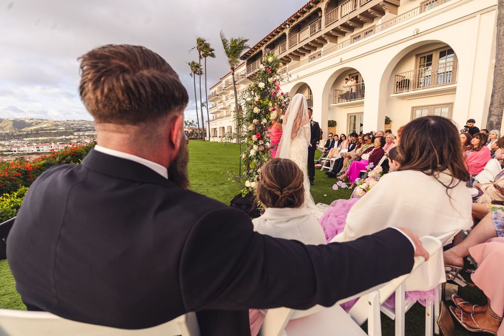 Groom and bride seated at outdoor wedding ceremony overlooking scenic coastal landscape at elegant venue.
