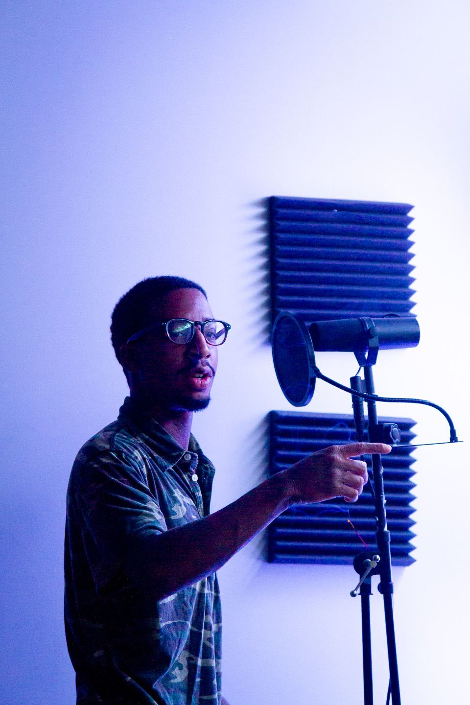 Silhouetted profile figure with glasses against blue background appears to be singing into a microphone with sound panels visible.