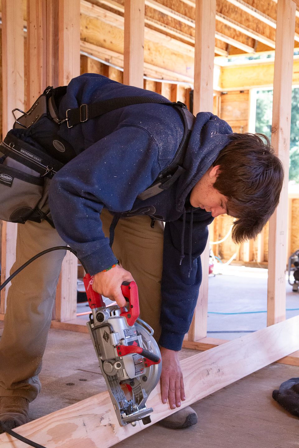 Construction worker using circular saw to cut lumber at residential building site during framing phase.