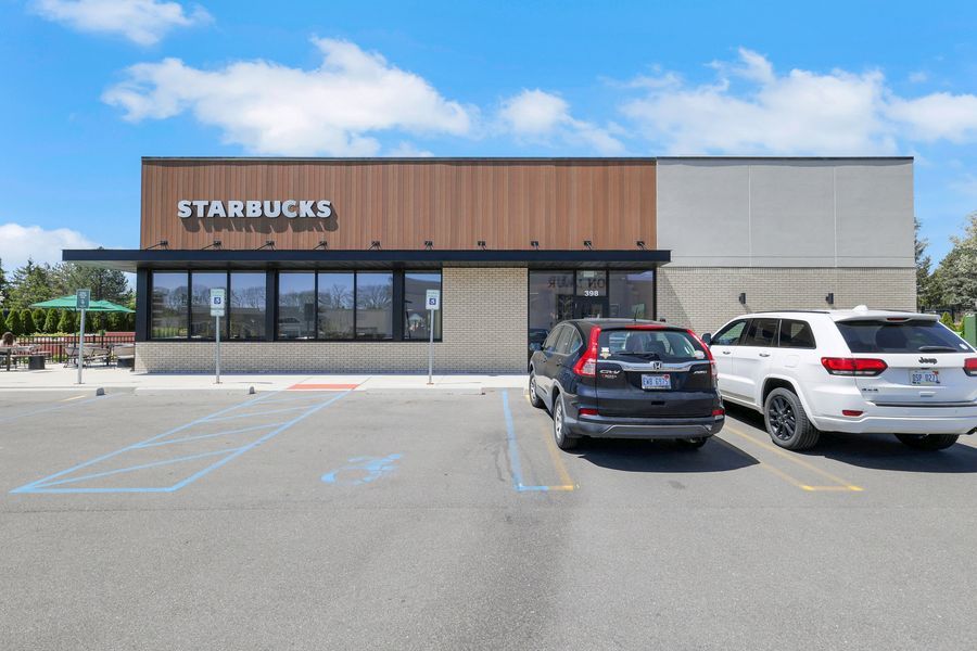 Starbucks Coffee drive-thru location with modern exterior, large parking lot, and parked SUVs on a sunny day.