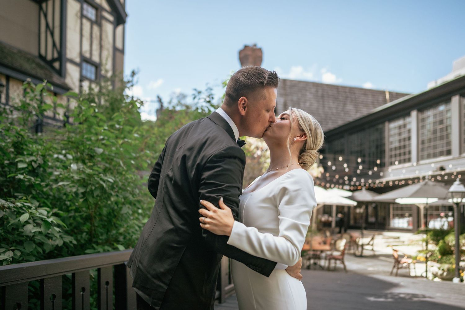 Groom carries bride in wedding dress on urban street with red bus and brick hotel building in background.