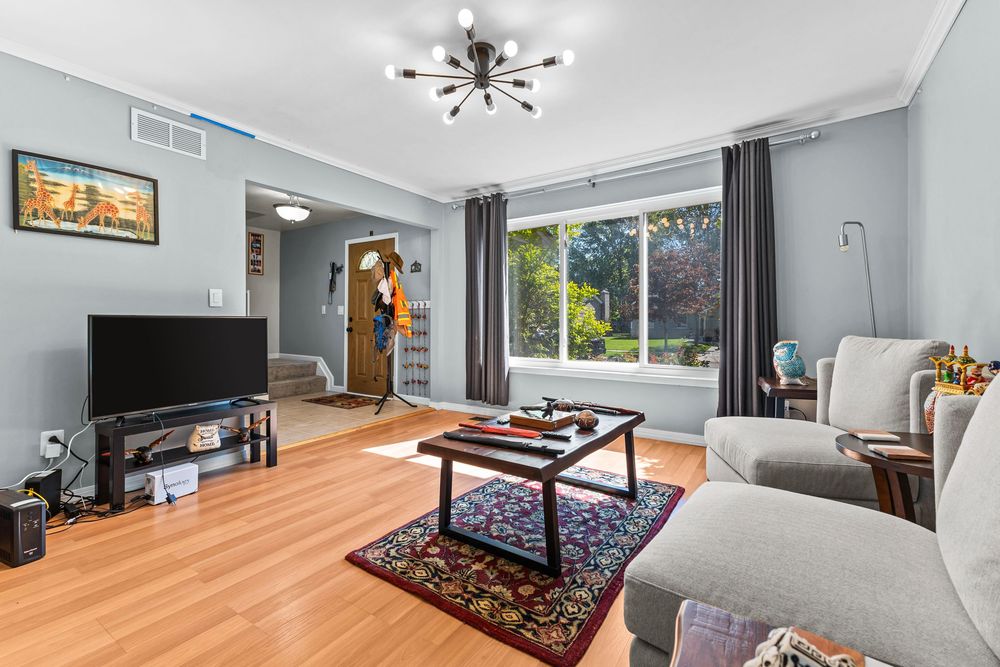 Open living room with hardwood floors, gray walls, large window, modern chandelier, and casual seating.