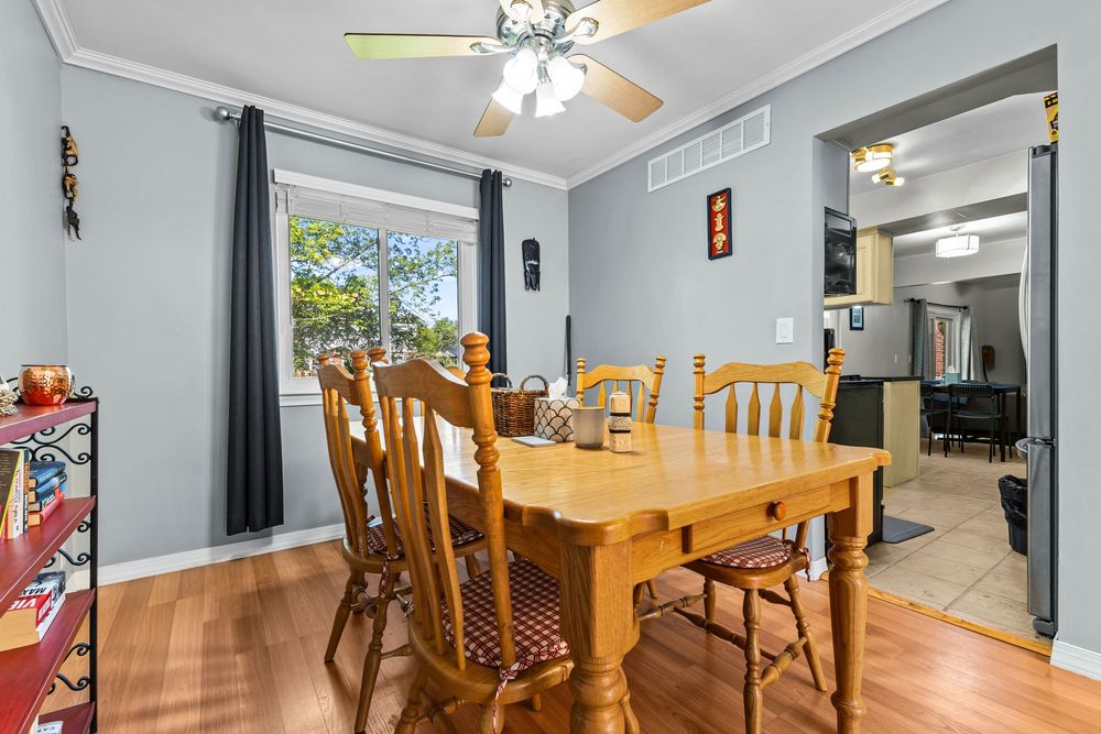 Dining room with wooden table, chairs, hardwood floors, ceiling fan, and gray walls with crown molding.