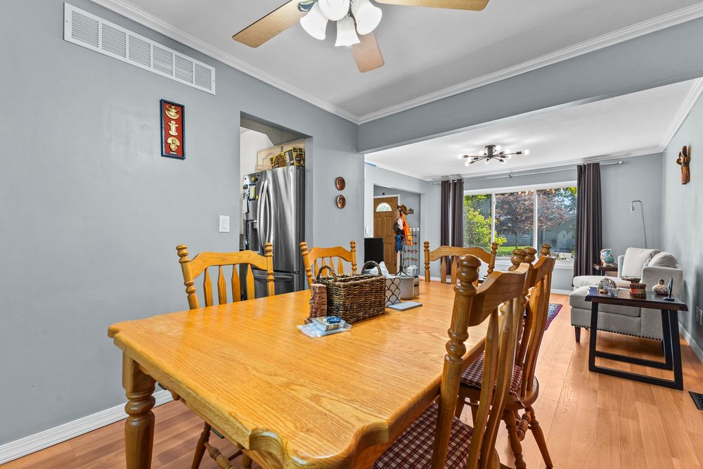 Dining area with wooden table and chairs, hardwood floors, ceiling fan, open to bright living room.