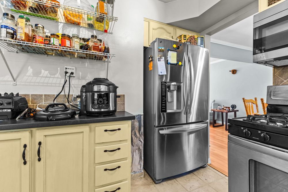 Kitchen corner with stainless French door refrigerator, cream cabinets, dark countertops, and small appliances.