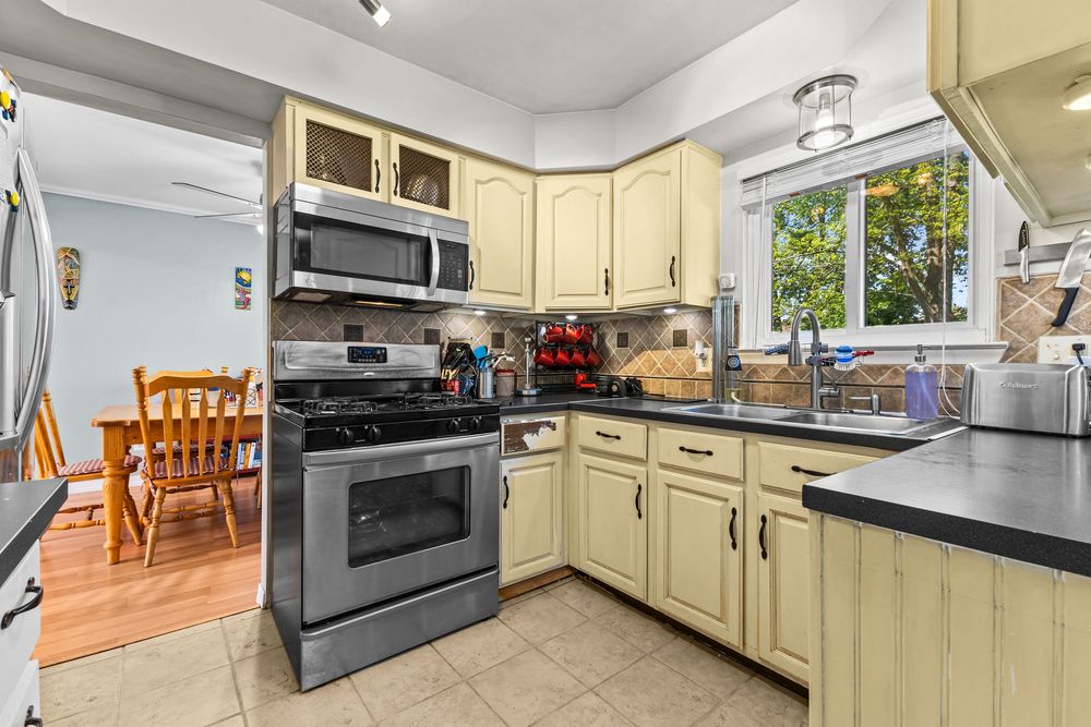 Modern kitchen with cream cabinets, stainless steel appliances, dark countertops, and tile flooring.