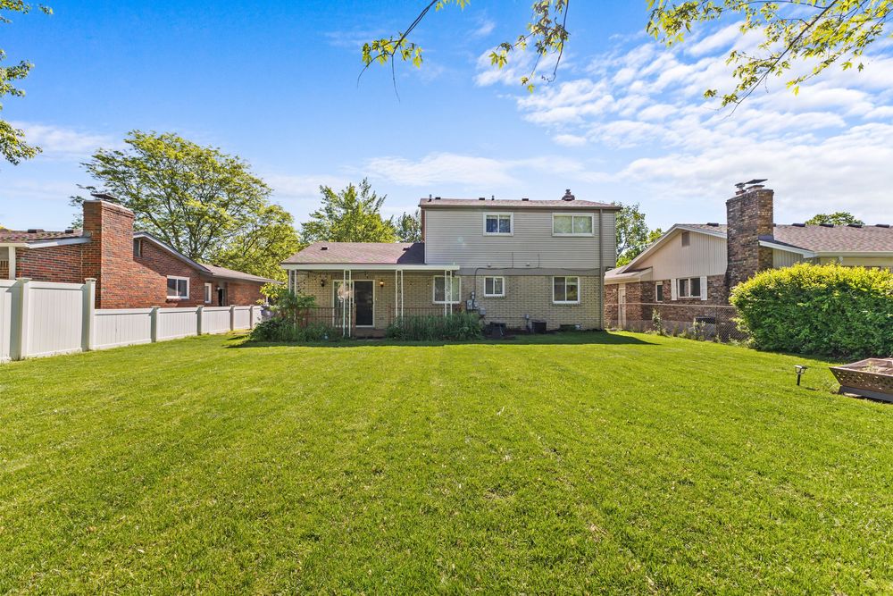 Expansive green backyard with white vinyl fence, mature trees, and rear view of a two-story suburban home.