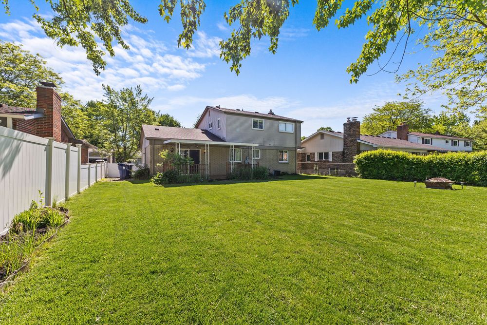 Spacious backyard with lush green lawn, white vinyl fence, and two-story home with deck on sunny day.