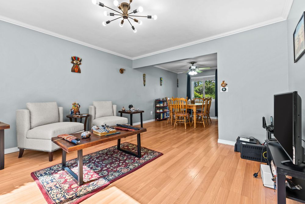 Bright living room with hardwood floors, gray walls, crown molding, and open view to dining area.