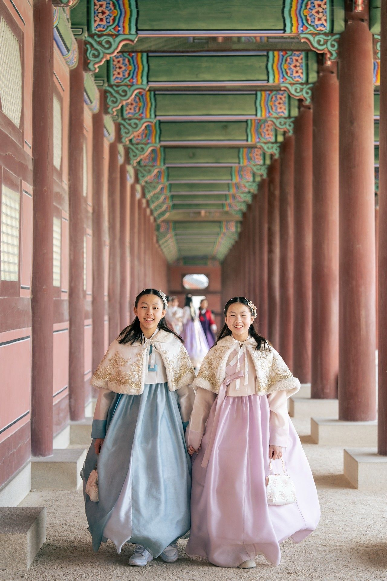Two women in traditional Korean hanbok attire pose in a colorful palace corridor at Gyeongbokgung, Seoul.