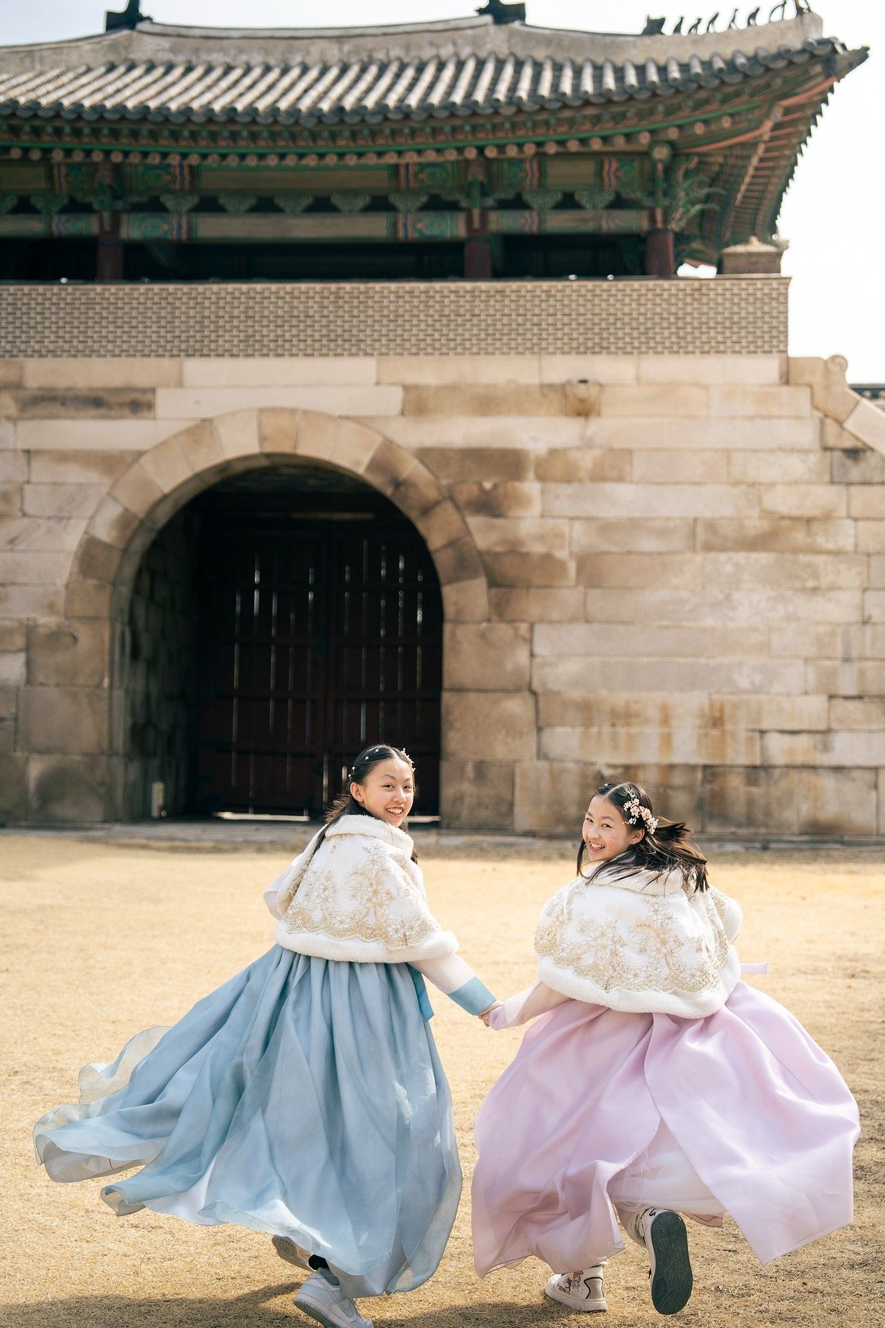 Two girls in traditional Korean hanbok dresses spin joyfully outside Gyeongbokgung Palace gates.