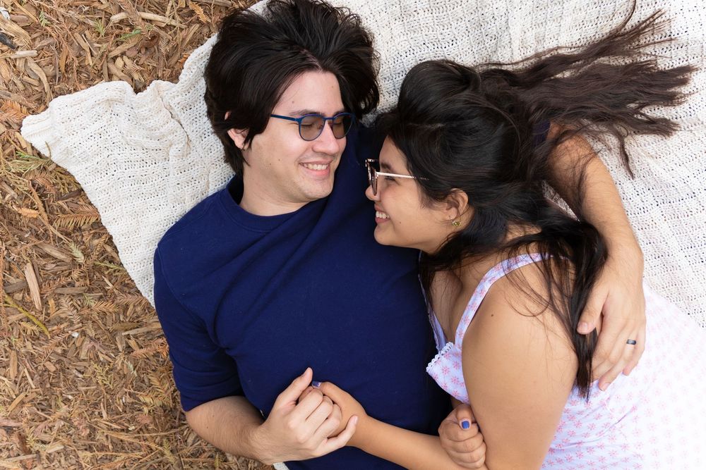 Engaged couple laying on a blanket, cuddling one another while smiling at each other