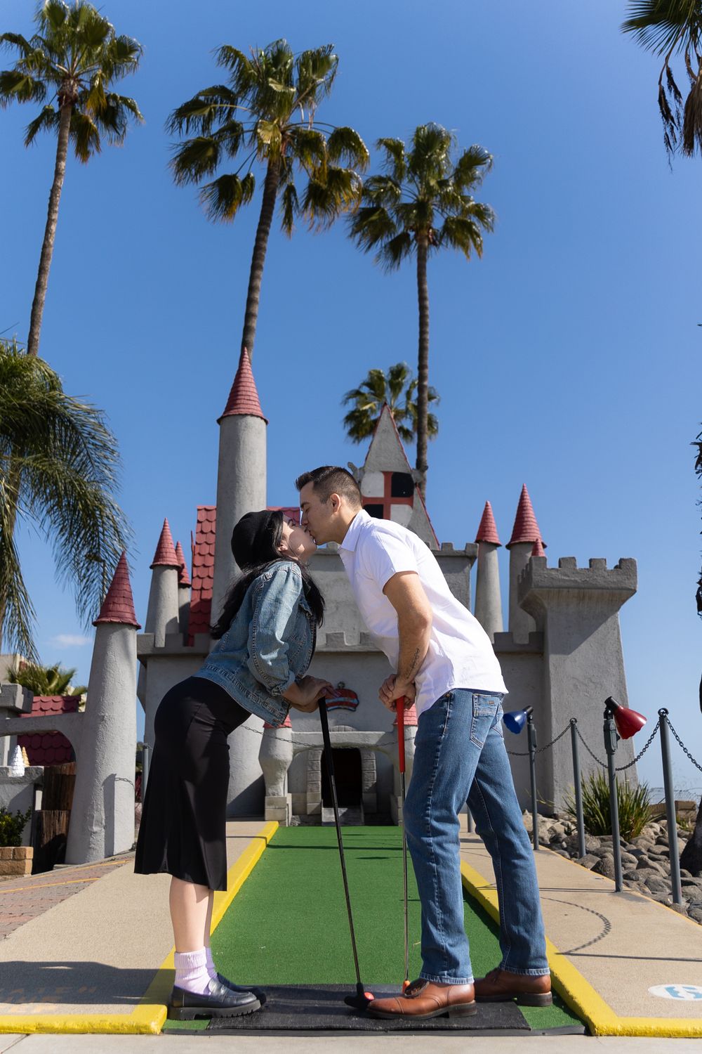 Couple playing mini golf while kissing during their engagement session.