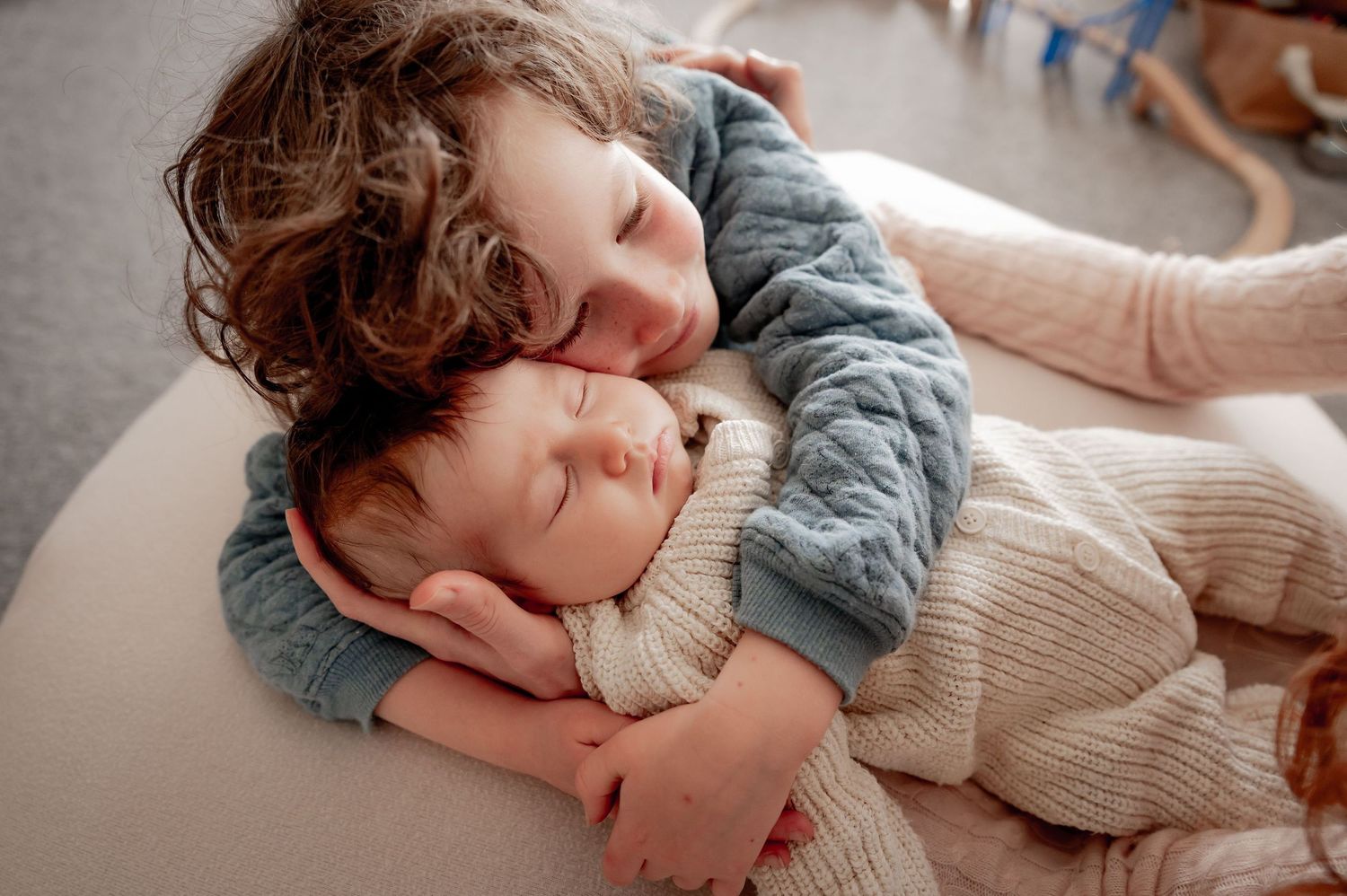 sibling cuddling newborn in family home