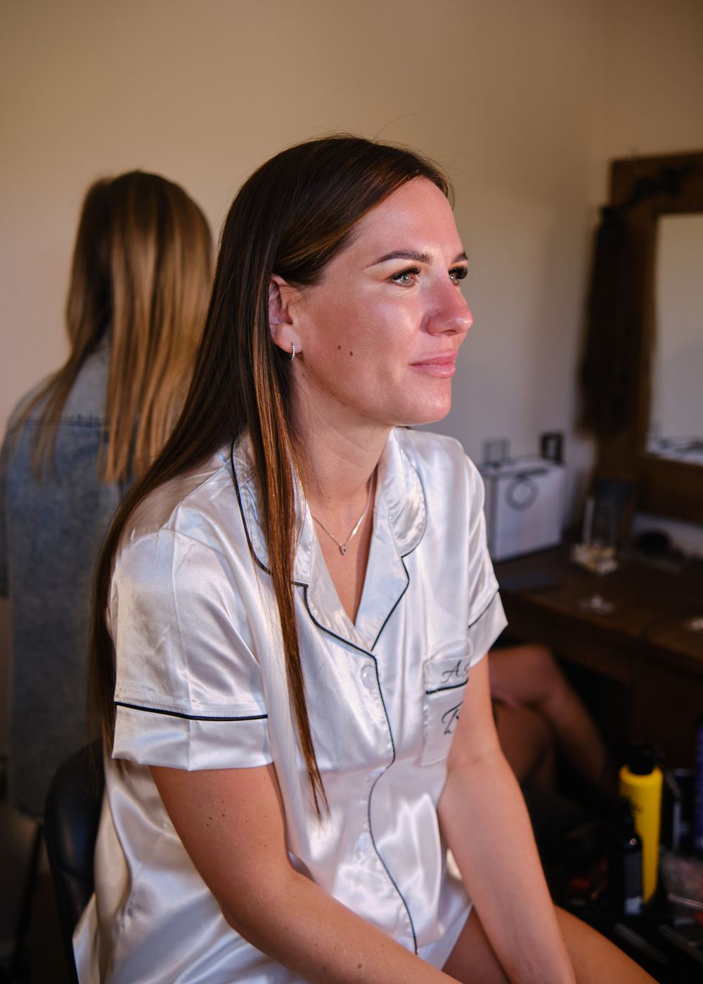 Bride-to-be in white satin pajamas getting hair and makeup done before wedding ceremony.