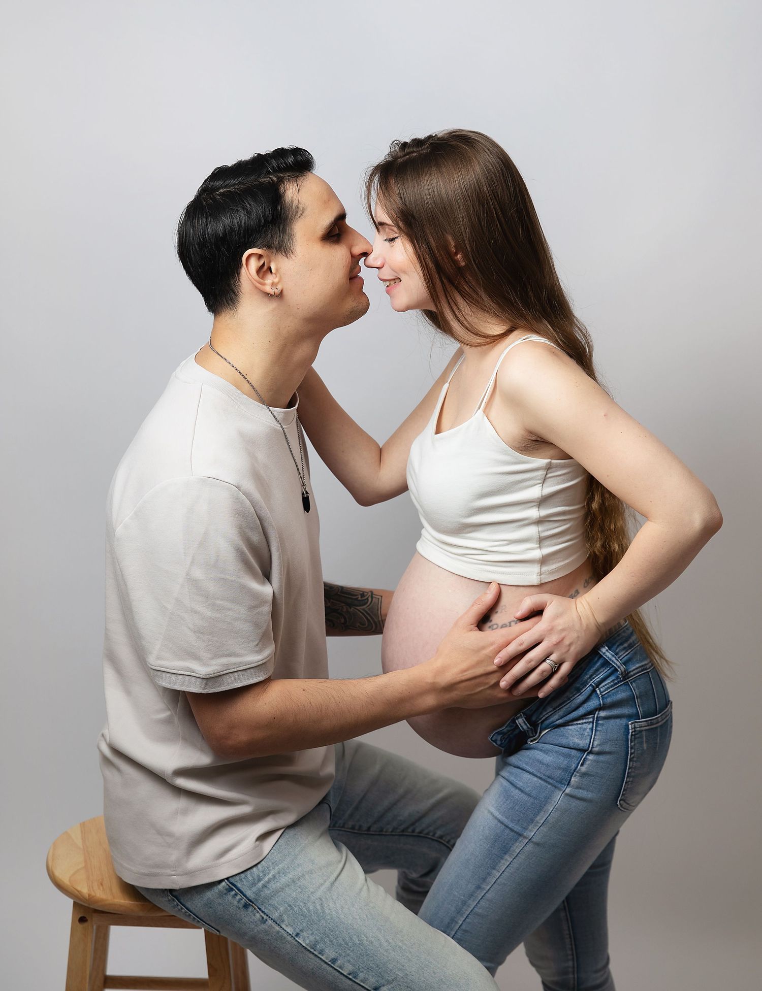 Couple sharing a tender moment during a maternity photo shoot in South East London. Man kissing pregnant woman's nose on grey background.