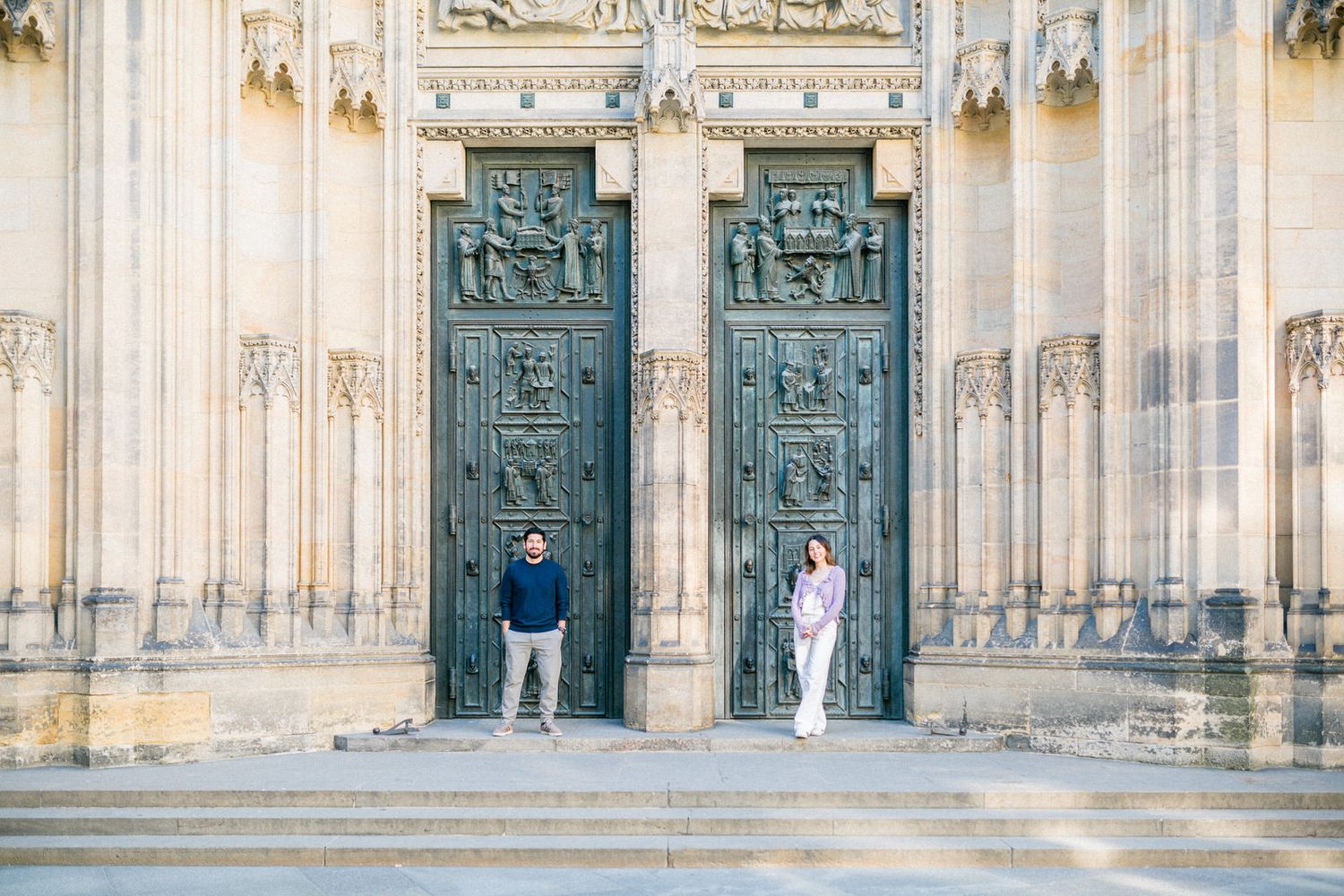 Two ornate turquoise doors with detailed carvings stand tall against a light stone cathedral facade in Prague.