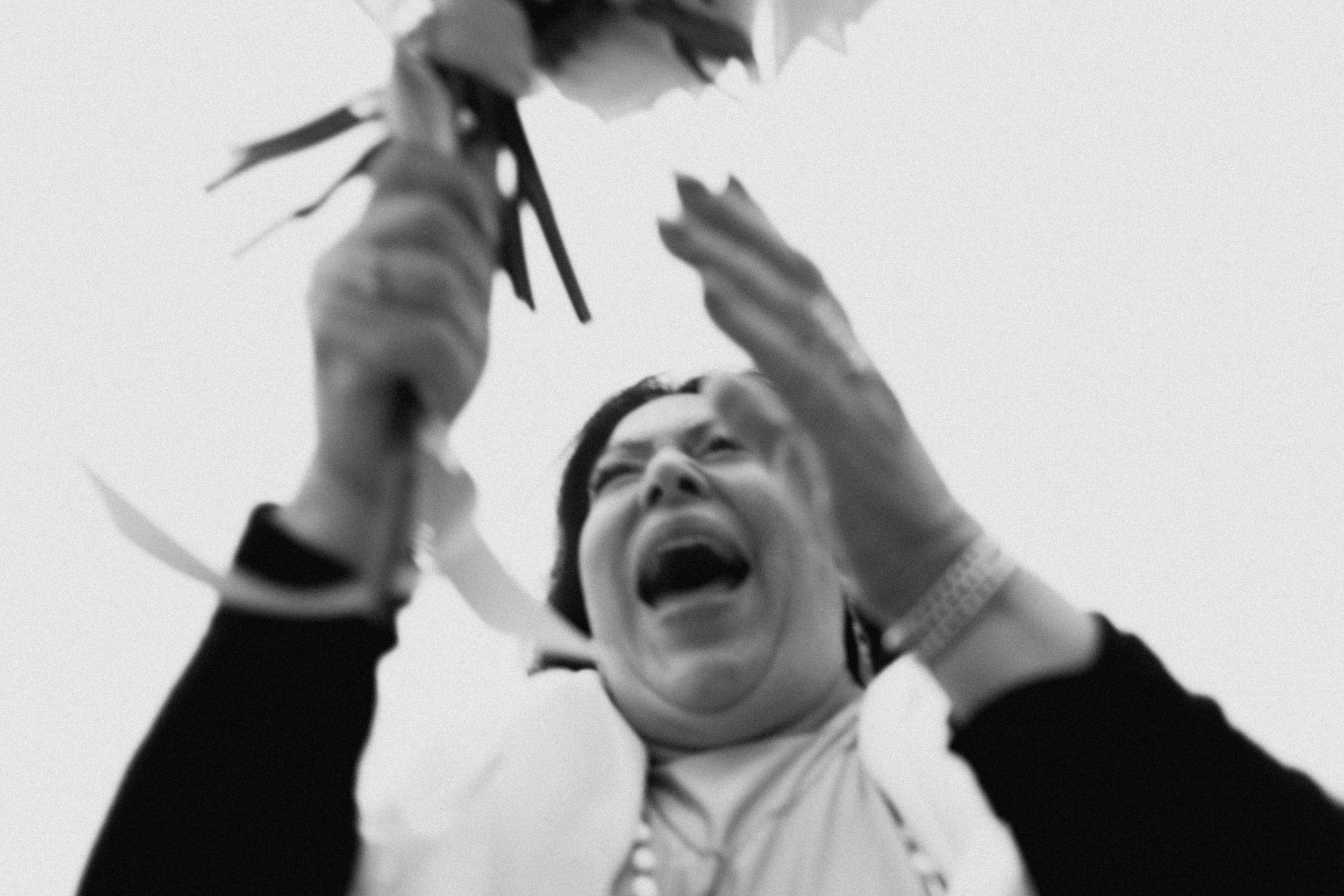 Black and white photo of a woman laughing joyfully while tossing flowers into the air outdoors.