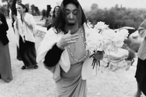 Black and white photo of emotional woman holding white bouquet at outdoor wedding ceremony.