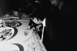 Black and white photo of a man in a suit leaning over a buffet table filled with food at a formal event.