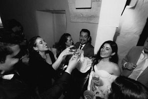 Black and white photo of wedding guests clinking glasses in a toast at a lively indoor reception celebration.