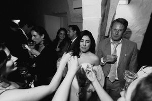 Black and white photo of guests mingling at an elegant evening party, with a woman in a strapless dress at center.