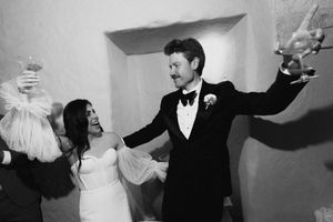 Black and white photo of a bride and groom celebrating joyfully at their wedding reception, raising glasses in a toast.
