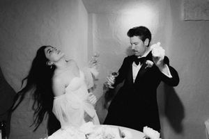 Black and white photo of bride and groom playfully smashing wedding cake at their elegant reception.