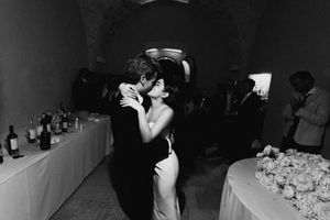 Black and white photo of a couple sharing a romantic kiss at an elegant wedding reception with floral arrangements.