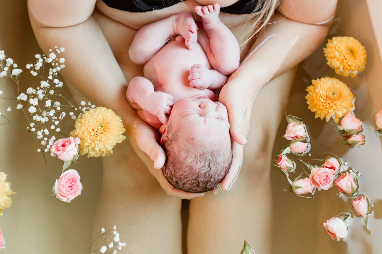 Overhead view of newborn baby cradled in mother's hands surrounded by colorful flowers.