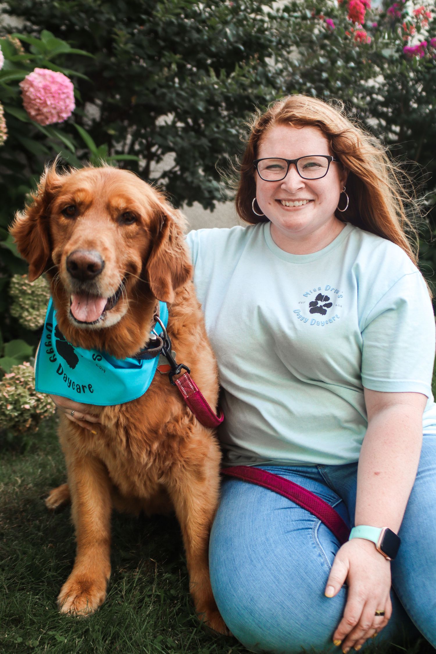 A happy golden retriever wearing a bandana poses with their owner in a garden setting.