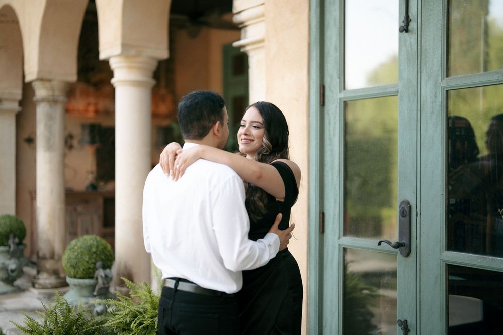 Couple embracing outdoors at elegant venue with columns, woman in black backless dress, man in white shirt.