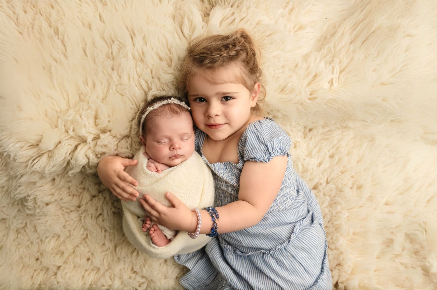 Sweet sisters cuddle against a soft white wool backdrop during a newborn sessions at Charlottesville baby and family photography studio.