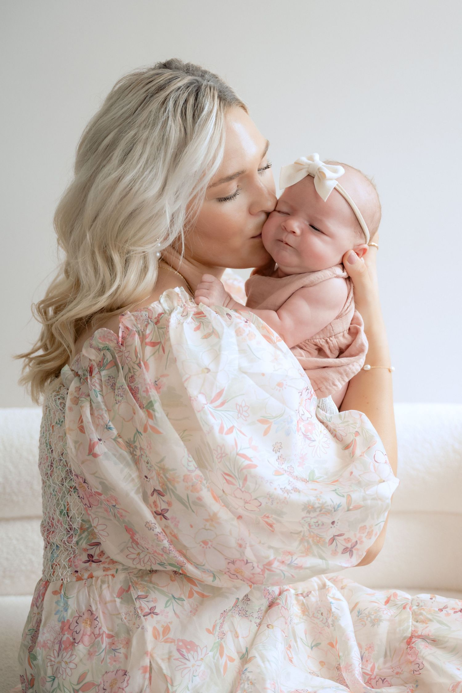 mom in a flowy pink and white dress kissing newborn baby on the cheek during in-studio lifestyle newborn session in stillwater, mn