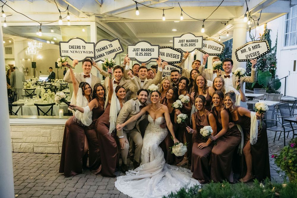 Wedding party poses with fun signs outside a venue Meson Sabika in Naperville, bridesmaids in brown dresses with bride and groom centered.