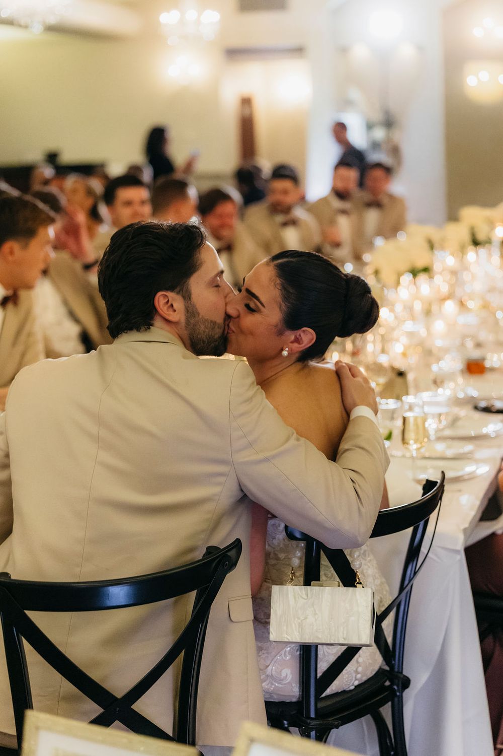 A bride and groom share a romantic kiss at their wedding reception dinner table surrounded by  guests at Meson Sabika in Naperville