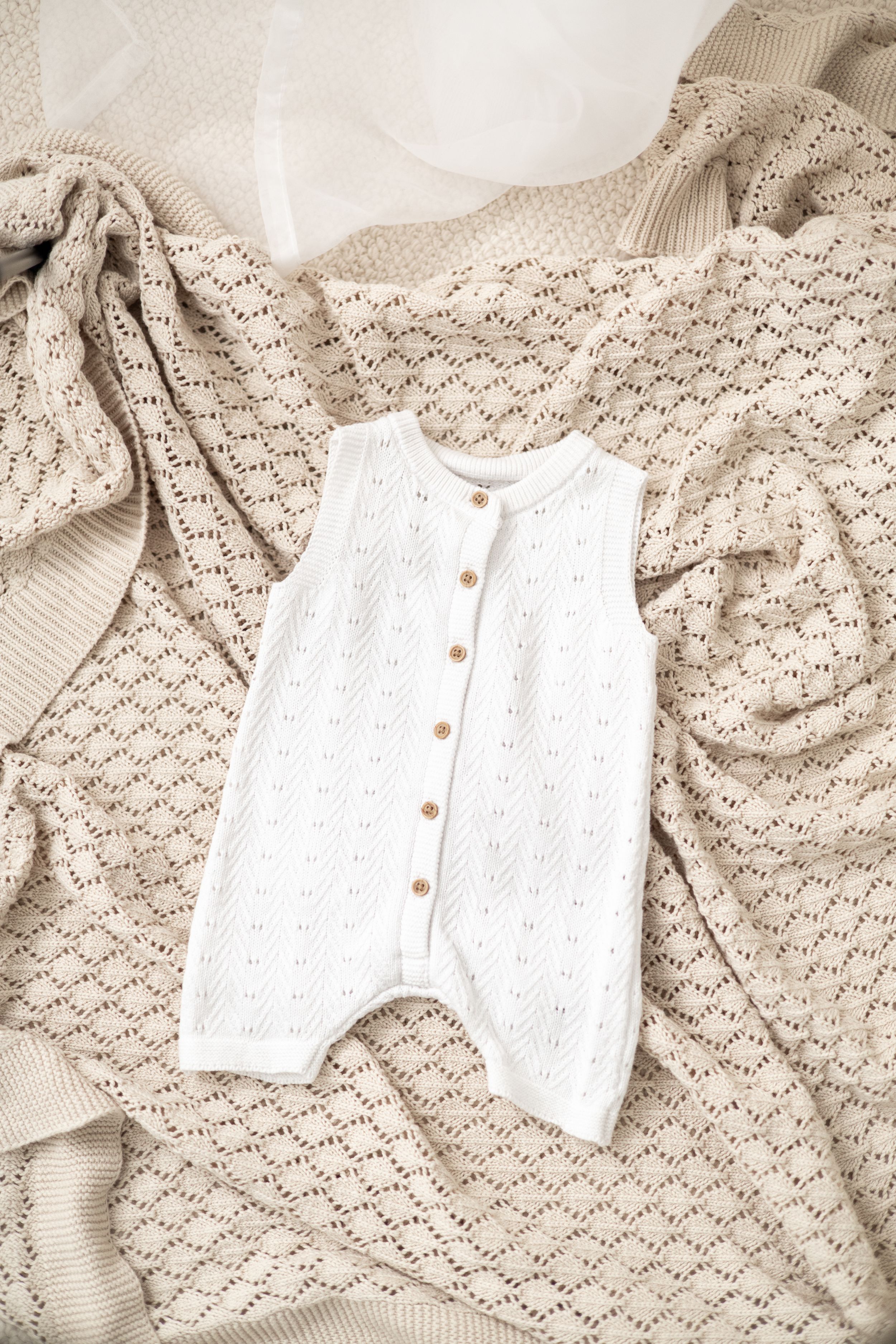 White knit baby romper with wooden buttons displayed on a beige lace blanket Newborn photographer Nottingham