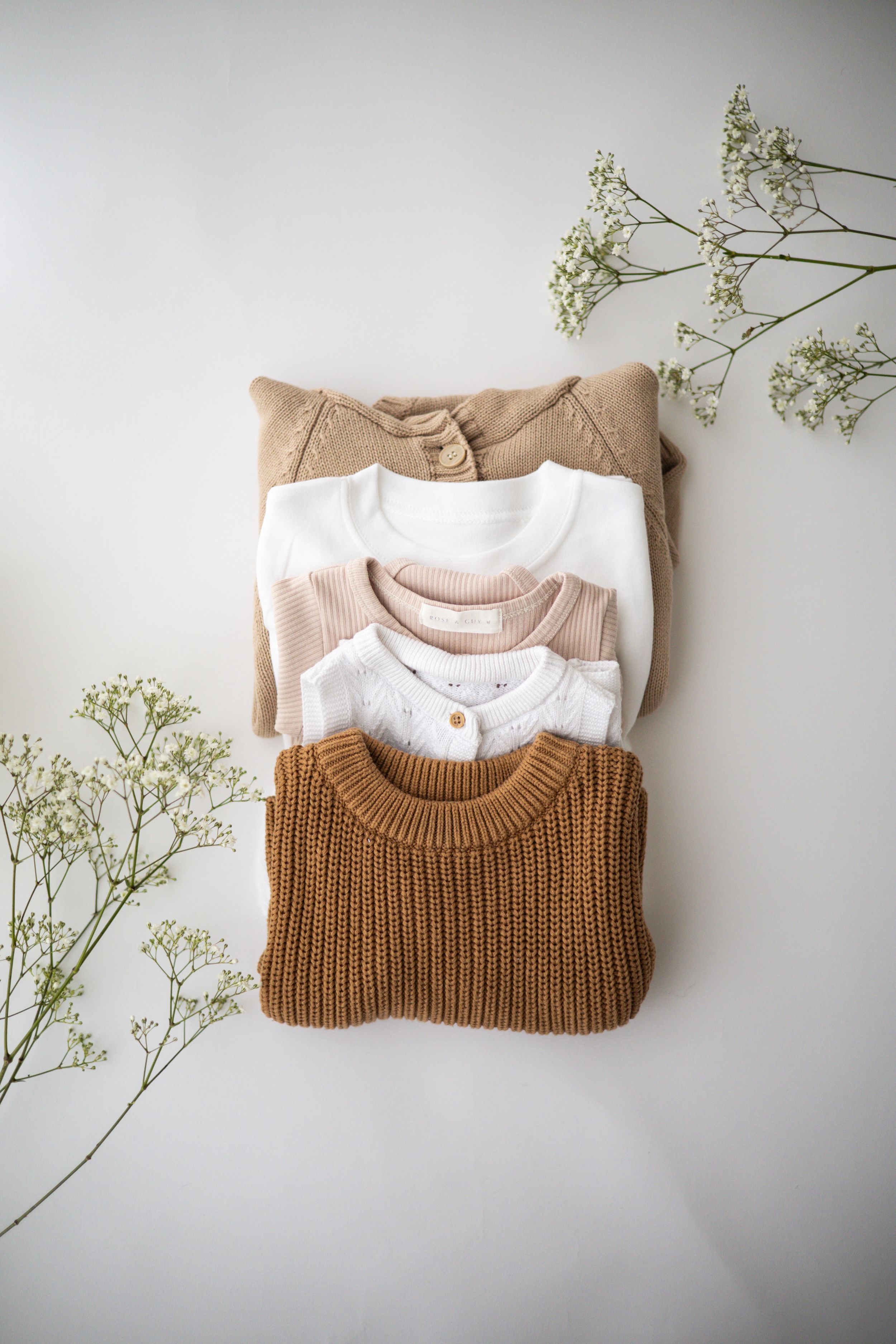 Stack of folded neutral-toned knit sweaters arranged with delicate white baby's breath flowers Newborn photographer Nottingham