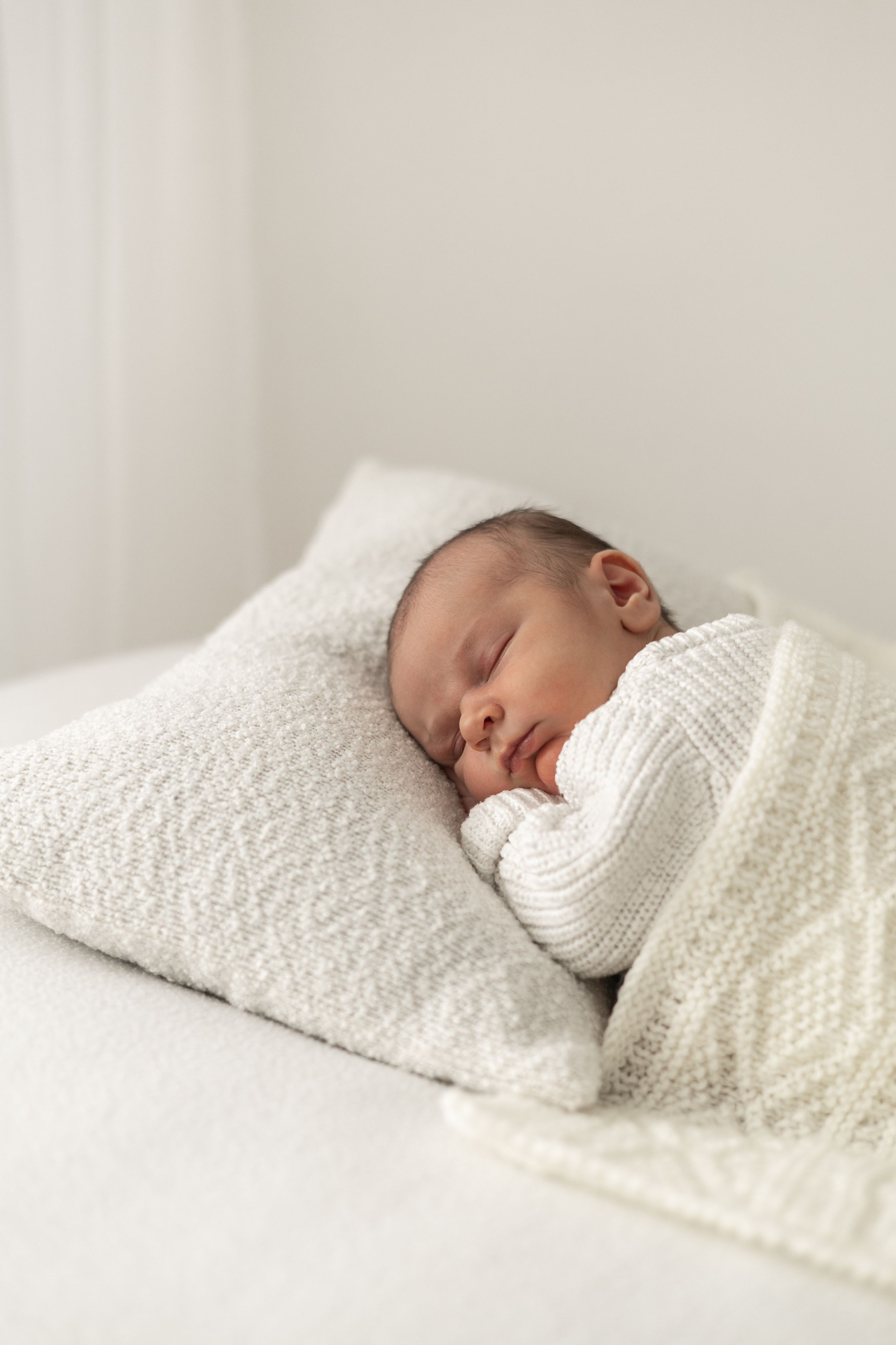 Peaceful newborn baby sleeping on a white pillow wrapped in a cozy knit blanket Newborn photographer Nottingham
